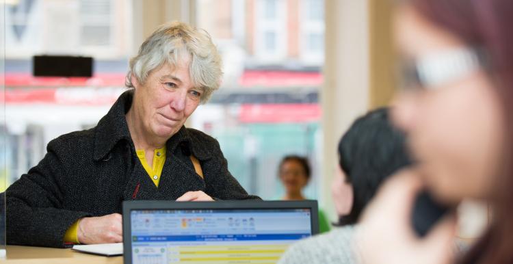 Older woman at a GP reception desk trying to book a GP appointment.