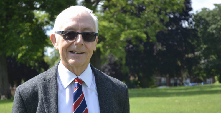 A picture of Alan smiling at the camera, standing in a park on a lovely sunny day.