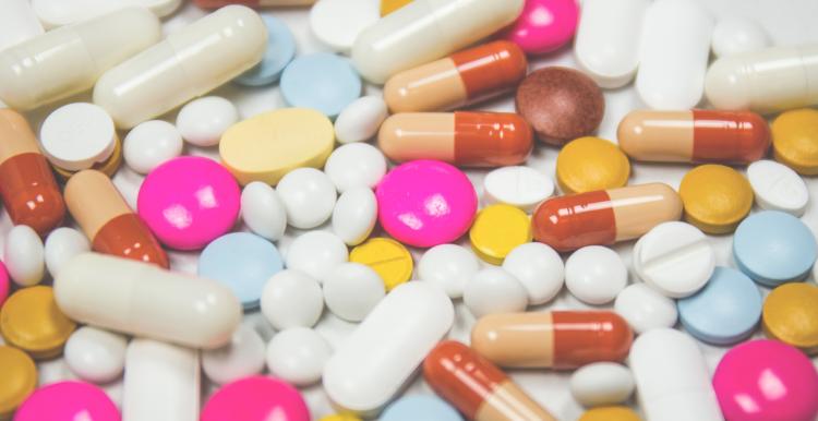 A variety of pills spread out on a white worktop. 